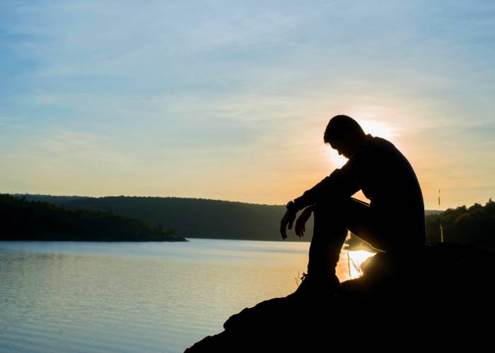 A guy sits at sunset by the river